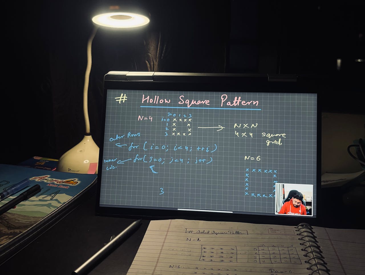 A dimly lit home study setup with laptop displaying coding notes on a hollow square pattern.